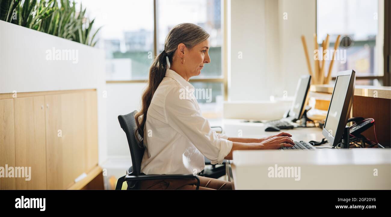 Vista laterale della donna che lavora al computer alla scrivania dell'ufficio. Dirigente femminile che utilizza il computer al lavoro Foto Stock