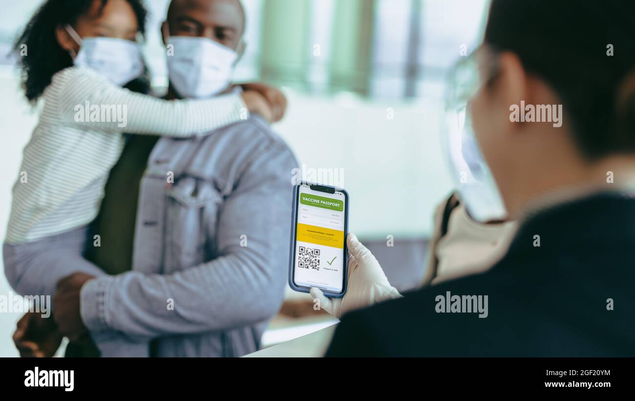 Personale dell'aeroporto che detiene il passaporto per il vaccino sul telefono cellulare del passeggero al banco del check-in. Personale di terra che esamina il certificato di vaccino del viaggiatore il Foto Stock