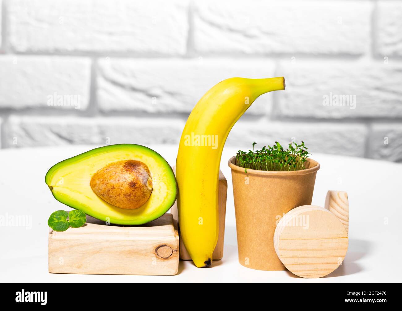 Vita morta creativa con avocado, banana e micro verde sul backgroun con stand e podi in legno. Equilibrio cibo sano. Dadi bilanciati Foto Stock