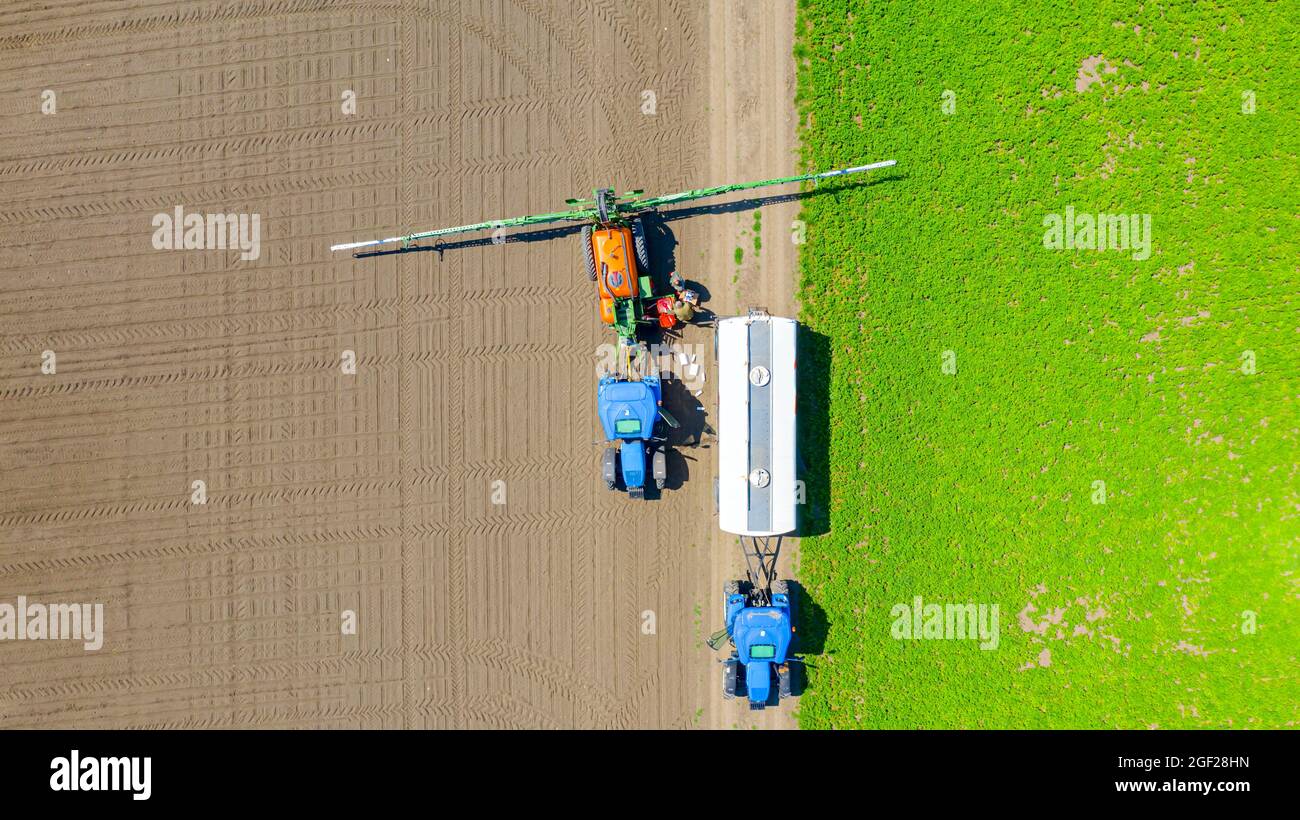 Vista dall'alto, vista dall'alto su due agricoltori durante la preparazione, la miscelazione di prodotti chimici e il riempimento del serbatoio dell'irroratrice con acqua dalla cisterna agricola. Foto Stock