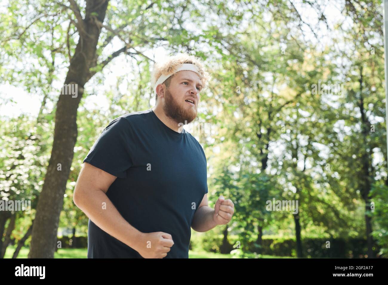 Uomo sovrappeso in abbigliamento sportivo che corre da solo nel parco Foto Stock