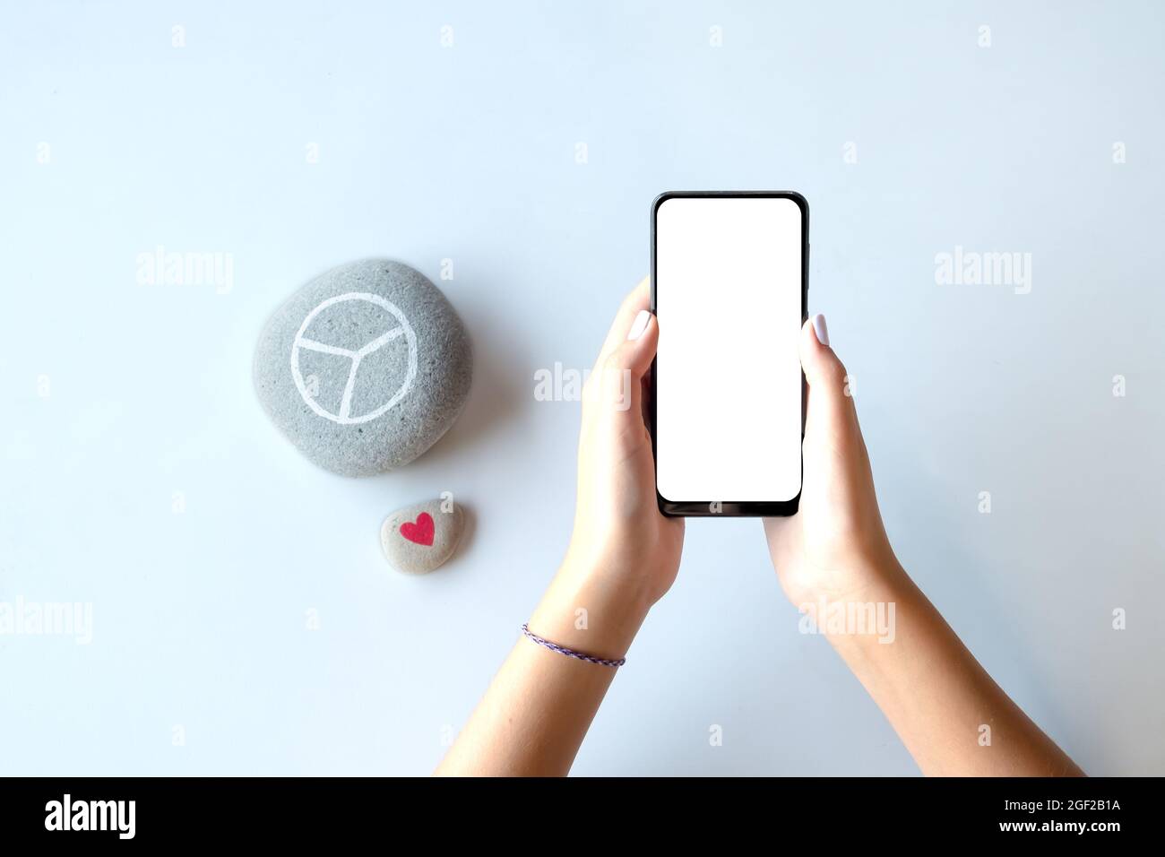 Le giovani mani femminili tengono uno smartphone con schermo vuoto. Modello utile per la presentazione di siti Web o app. Simboli di pace e di amore dalla parte. Foto Stock