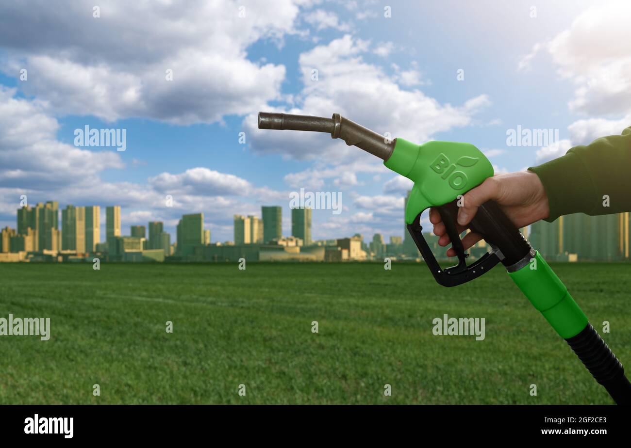 Mano con ugello carburante con iscrizione BIO sullo sfondo verde eco città. Concetto di biocarburante Foto Stock