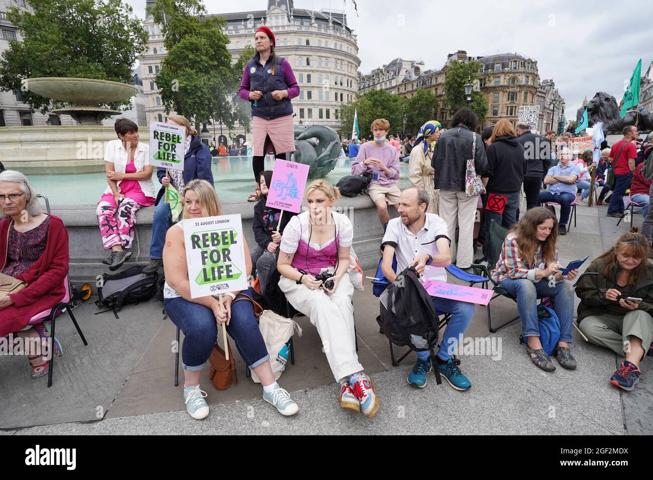 I dimostranti siedono con i segni durante una protesta dei membri della ribellione di estinzione a Trafalgar Square, nel centro di Londra, all'inizio di una prevista azione di due settimane da parte del gruppo di protesta del cambiamento climatico. Data foto: Lunedì 23 agosto 2021. Foto Stock