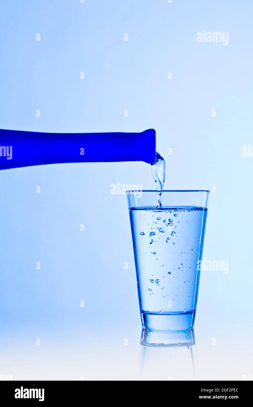 Un bicchiere viene riempito con acqua da una bottiglia blu Foto Stock