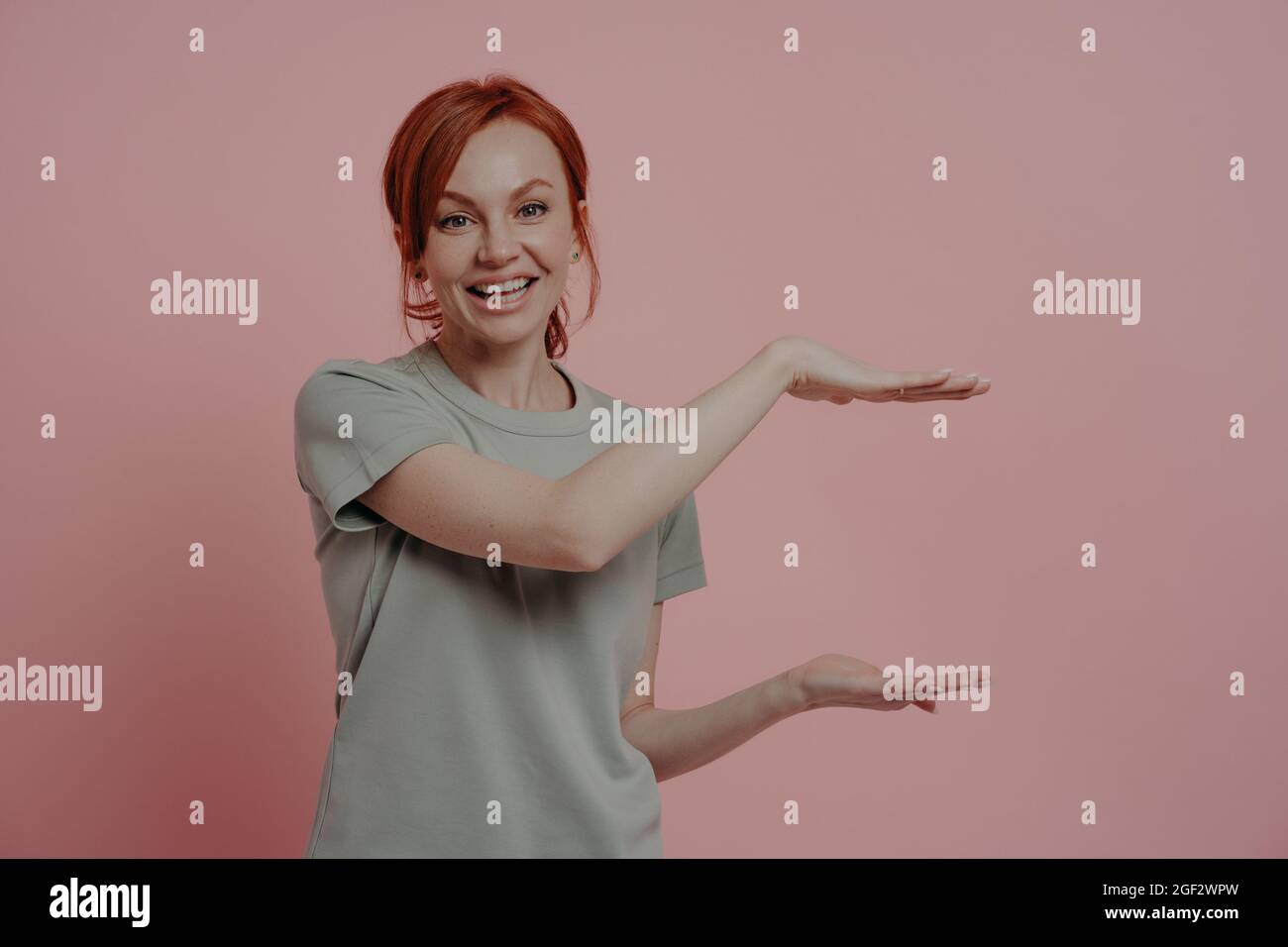 Giovane donna piacevole con capelli rossi che mostra un prodotto di grandi dimensioni o qualcosa di grande con le mani Foto Stock