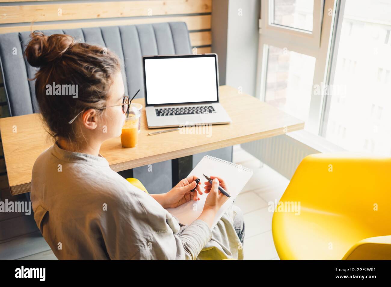 Donna che studia a distanza con un blocco note e un computer portatile, seduto in un bar e ascoltando un corso online o partecipando a una conferenza o seminario educativo Foto Stock