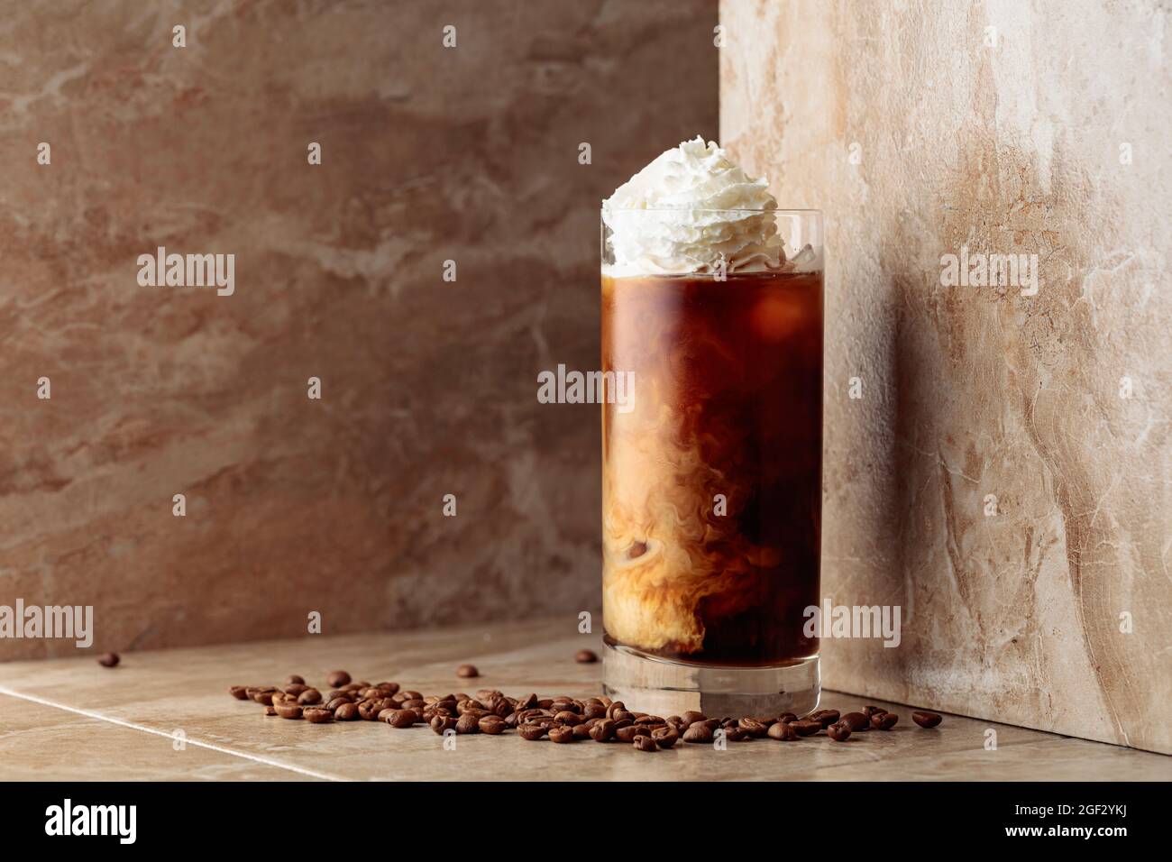 Caffè ghiacciato con panna su un tavolo in ceramica beige con chicchi di caffè. Spazio di copia. Foto Stock