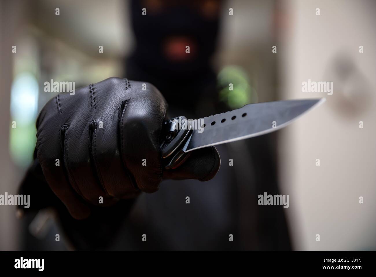 Burglar con balaclava, tenendo un coltello in mano guantata, concetto di rapina armato. Ladro minacciare con un pugnale, sfocatura sfondo interno, primo piano vista. Foto Stock