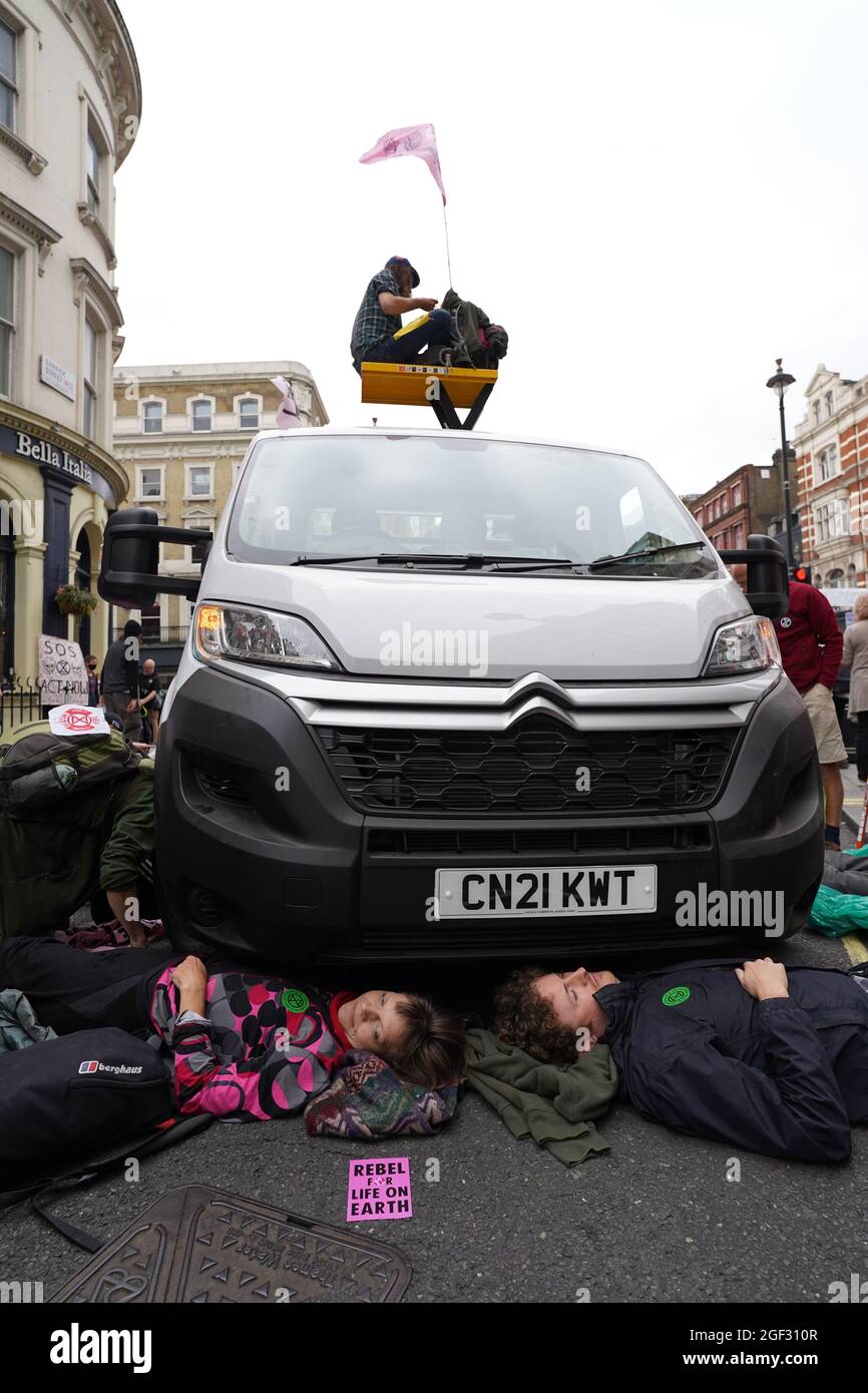 I dimostranti si posizionano sotto un furgone durante una protesta dei membri della ribellione di estinzione vicino a Covent Garden, nel centro di Londra, all'inizio di due settimane di azione previste dal gruppo di protesta per il cambiamento climatico. Data foto: Lunedì 23 agosto 2021. Foto Stock