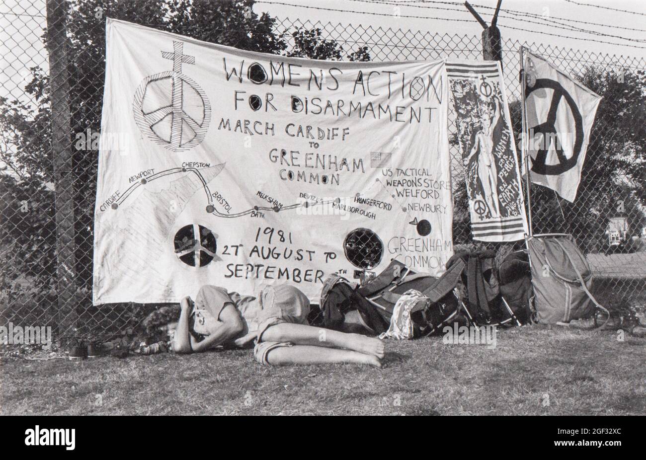 Greenham Common Peace Camp giorno 1. Arrivando a Greenham dopo aver marciato da Cardiff una donna riposa sotto le bandiere alla recinzione perimetrale del cancello principale. Foto Stock