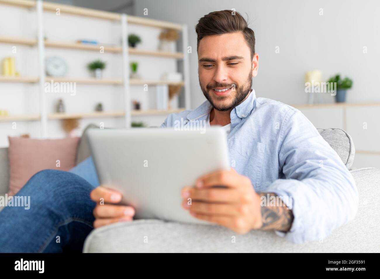 Primo piano dell'uomo caucasico che riposa sul divano con un tablet digitale, utilizzando una bella app mobile, interni domestici, spazio libero Foto Stock