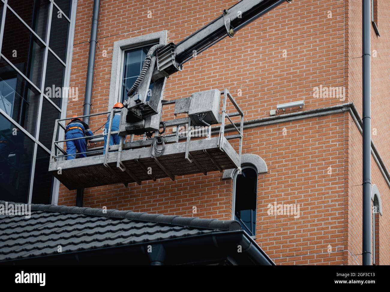 Lavoratori in facciata di riparazione hardhat dell'edificio in altezza nella culla di sollevamento. Lavori di finitura della facciata. Foto Stock