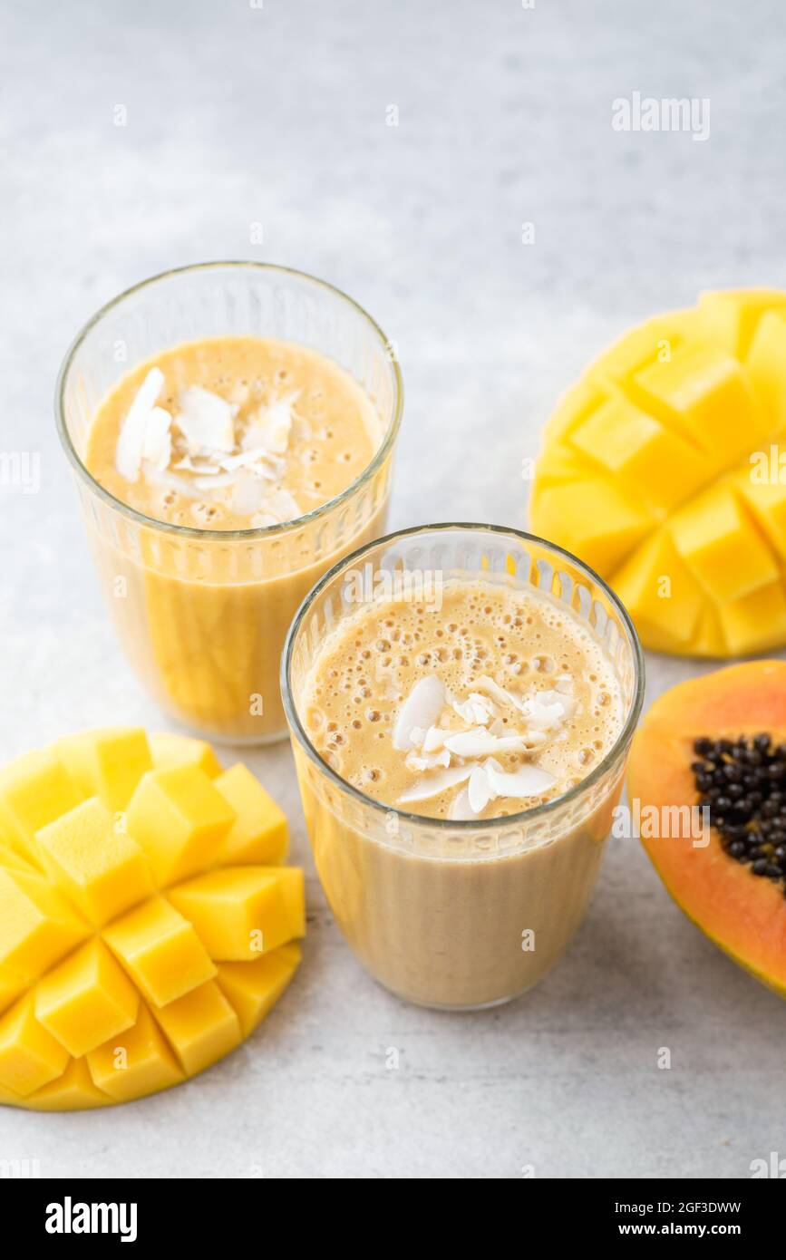 Frullato giallo di frutta tropicale di mango e papaya in un bicchiere da bere con carta che beve paglia Foto Stock