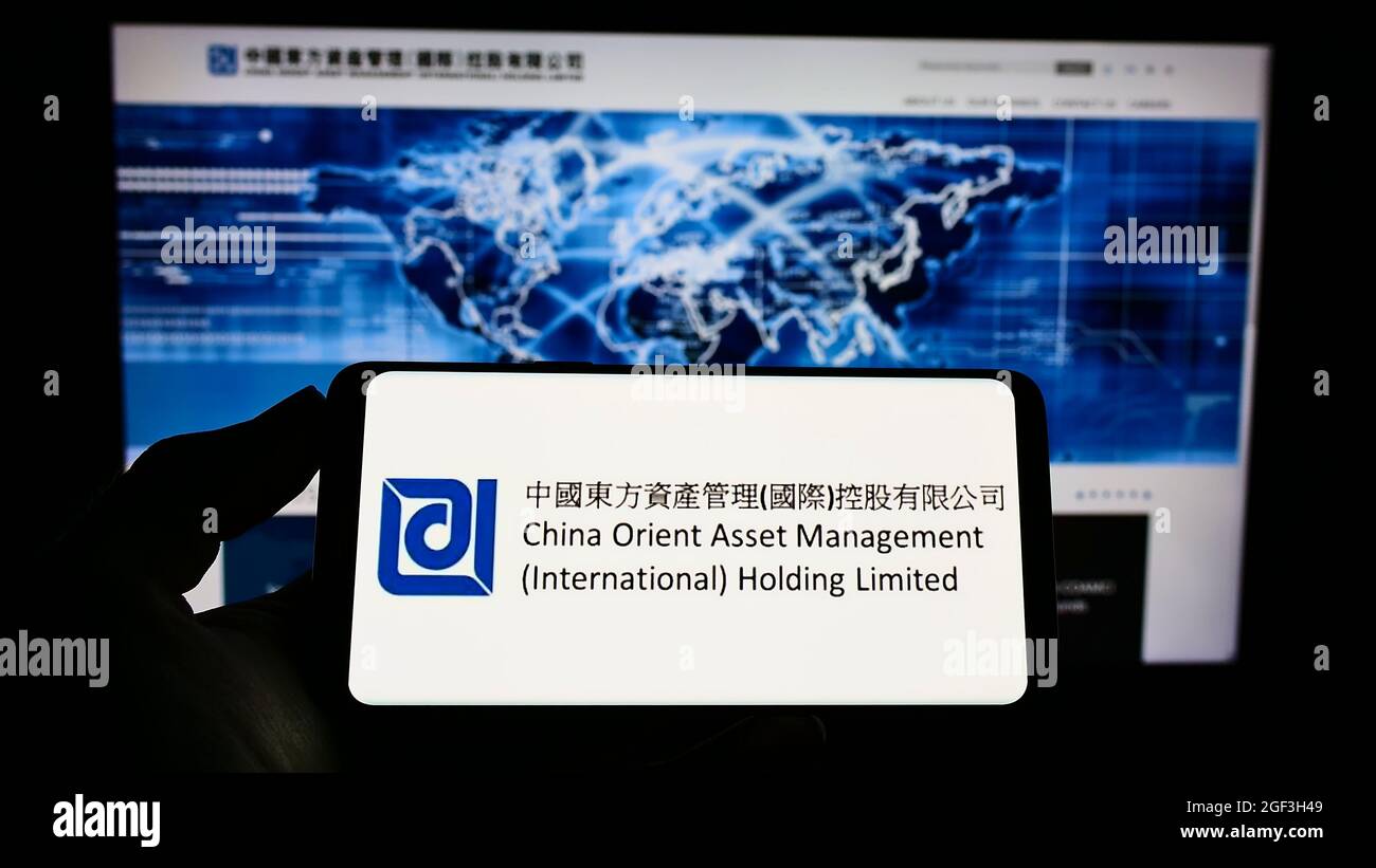 Persona che tiene il cellulare con il logo della società China Orient Asset Management Co. Ltd. Sullo schermo di fronte al sito web. Mettere a fuoco sul display del telefono. Foto Stock