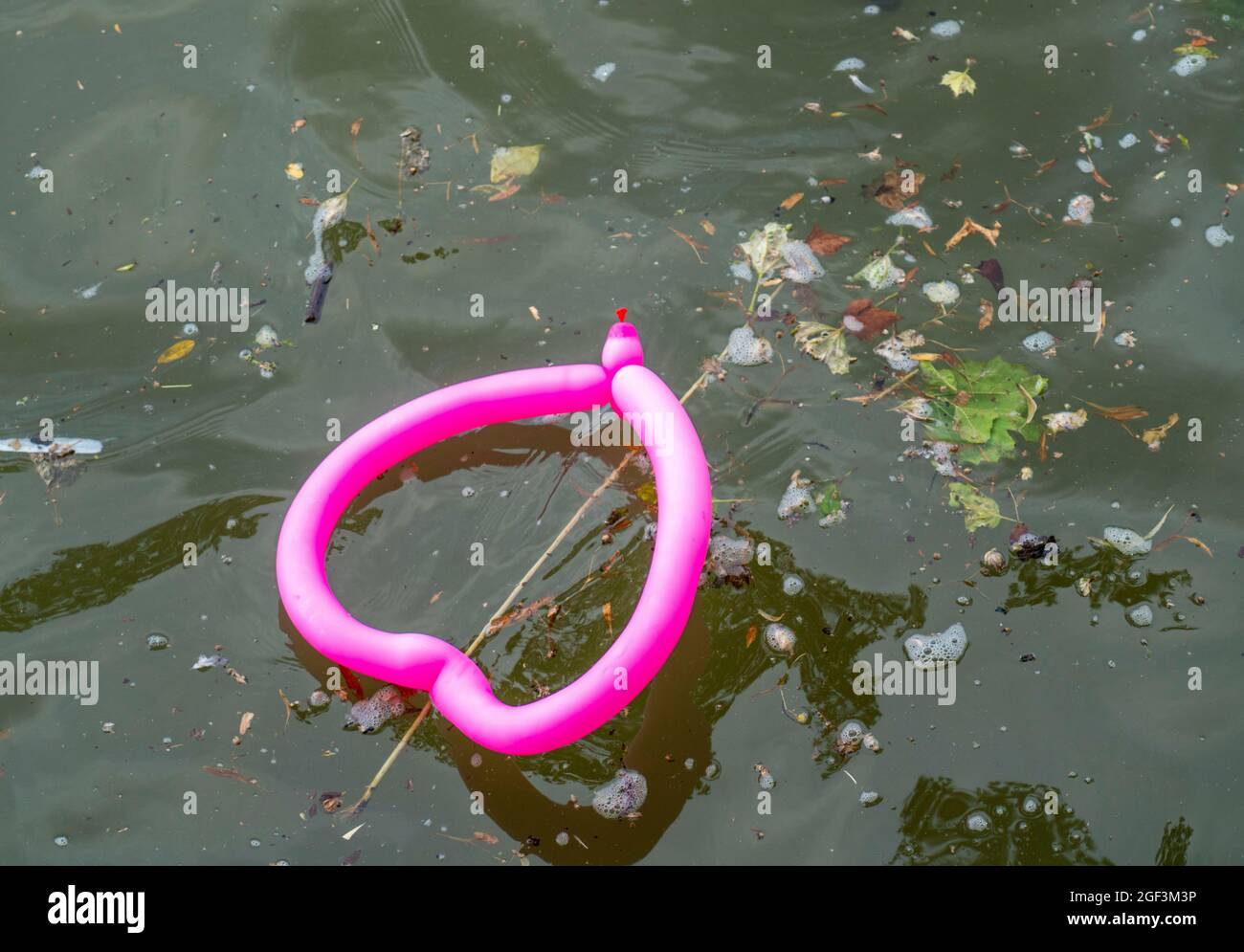 Palloncino rosa, a forma di cuore, galleggiante in un fiume sporco, Foto Stock
