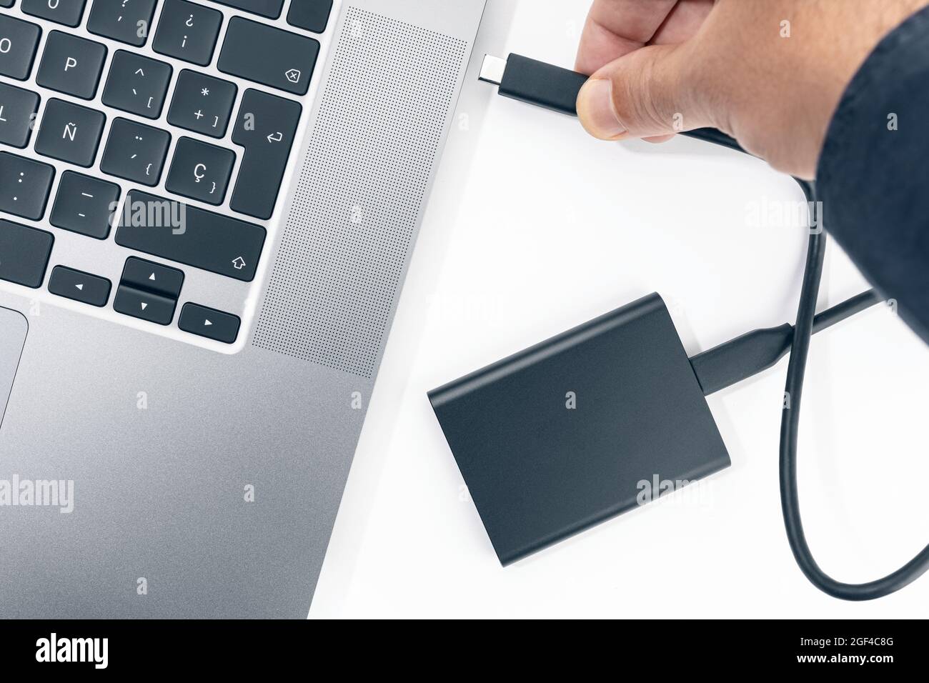 Collegamento manuale di un disco rigido esterno a un moderno computer portatile. Vista dall'alto Foto Stock
