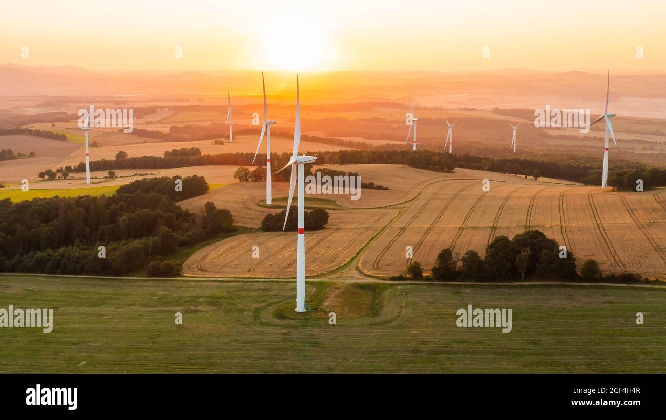 Vista panoramica di mulini a vento o turbine eoliche per la produzione di energia elettrica al tramonto sorprendente nel campo. Generazione di energia rinnovabile verde. Foto Stock