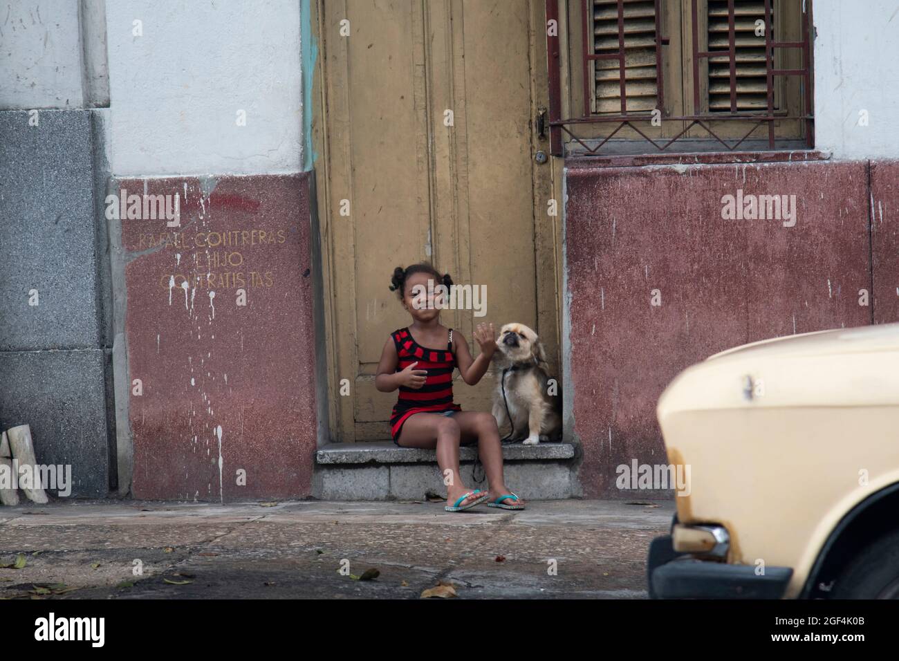 La giovane ragazza cubana sorride alla macchina fotografica con il suo cane per le strade di l'Avana, Cuba Foto Stock