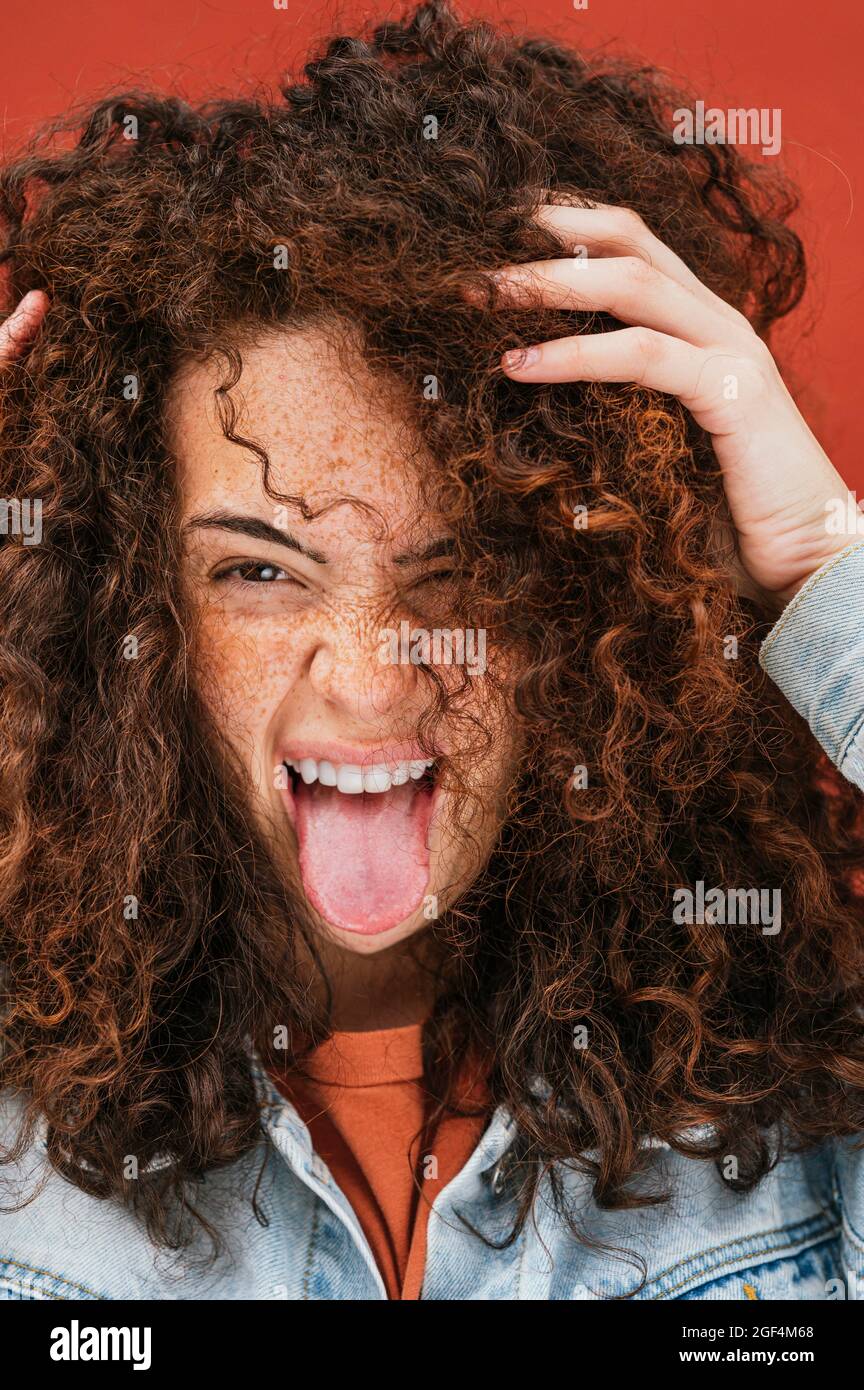 Giovane donna ricciola con le mani in capelli che si stacca fuori lingua Foto Stock