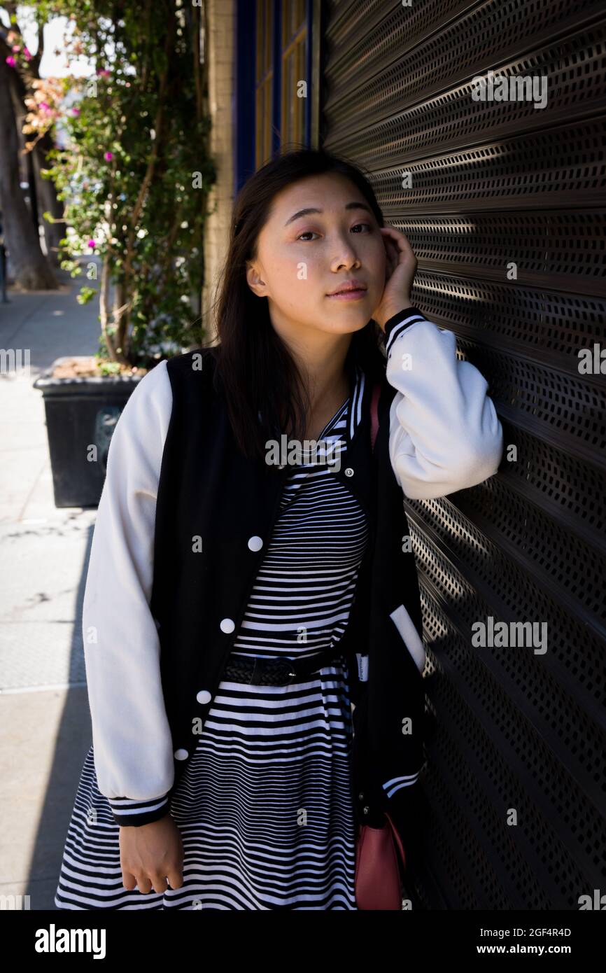 Ritratto di una bella giovane donna asiatica appoggiata su roll up porta di sicurezza in metallo a San Francisco Foto Stock