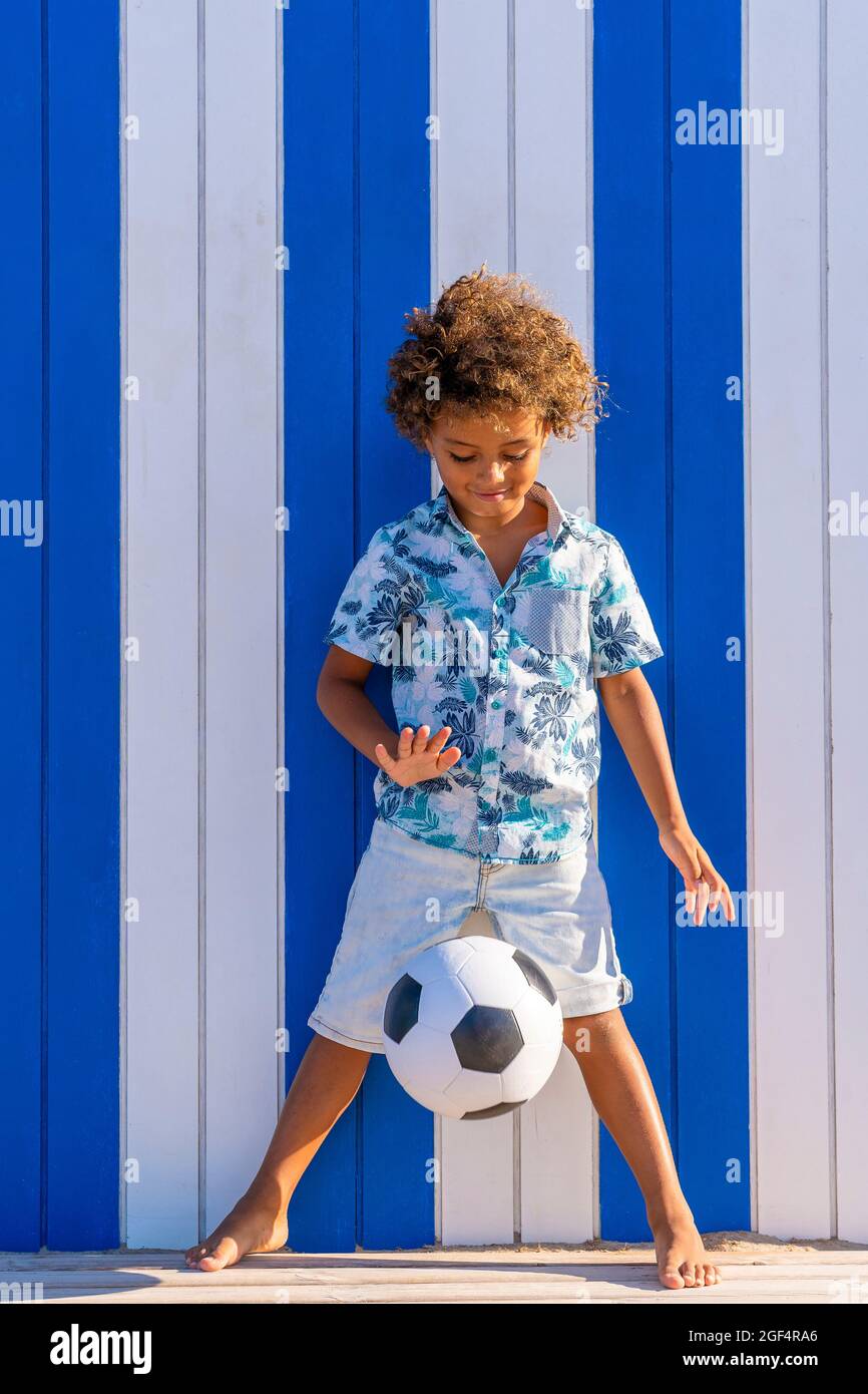 Ragazzo carino che gioca con la palla di calcio di fronte al muro a strisce Foto Stock