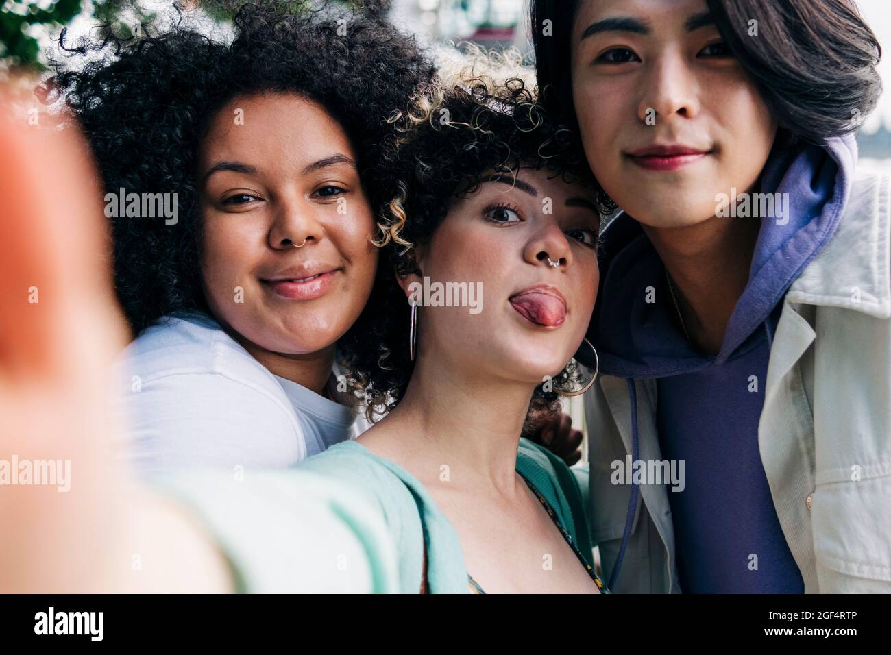 Giovane donna che attacca la lingua mentre prende selfie con amici multietnici Foto Stock