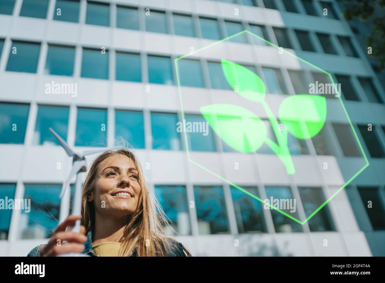 Donna sorridente con modello di mulino a vento guardando il logo della pianta vicino all'edificio Foto Stock