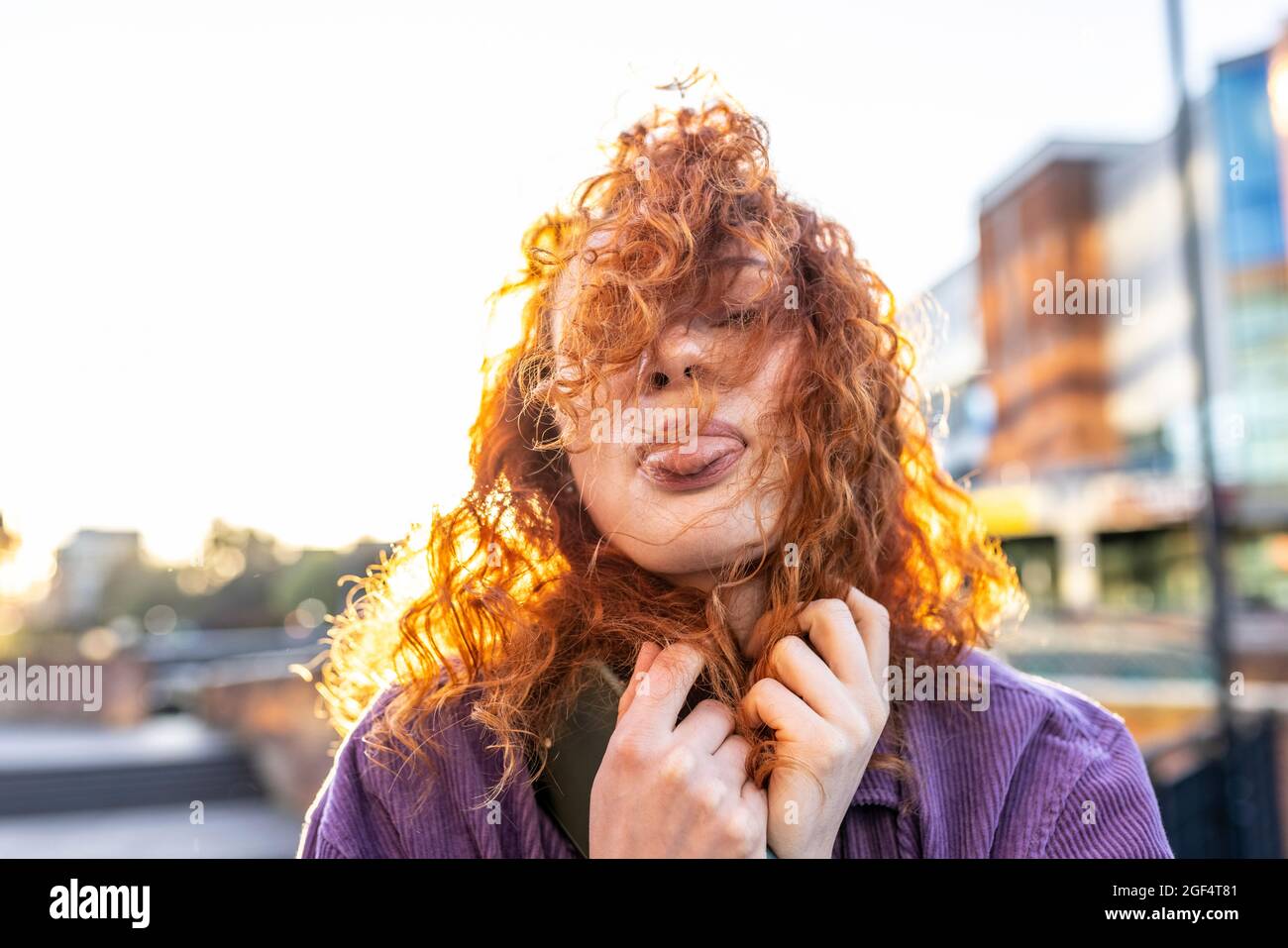 Donna dai capelli ricci che attacca la lingua durante il tramonto Foto Stock
