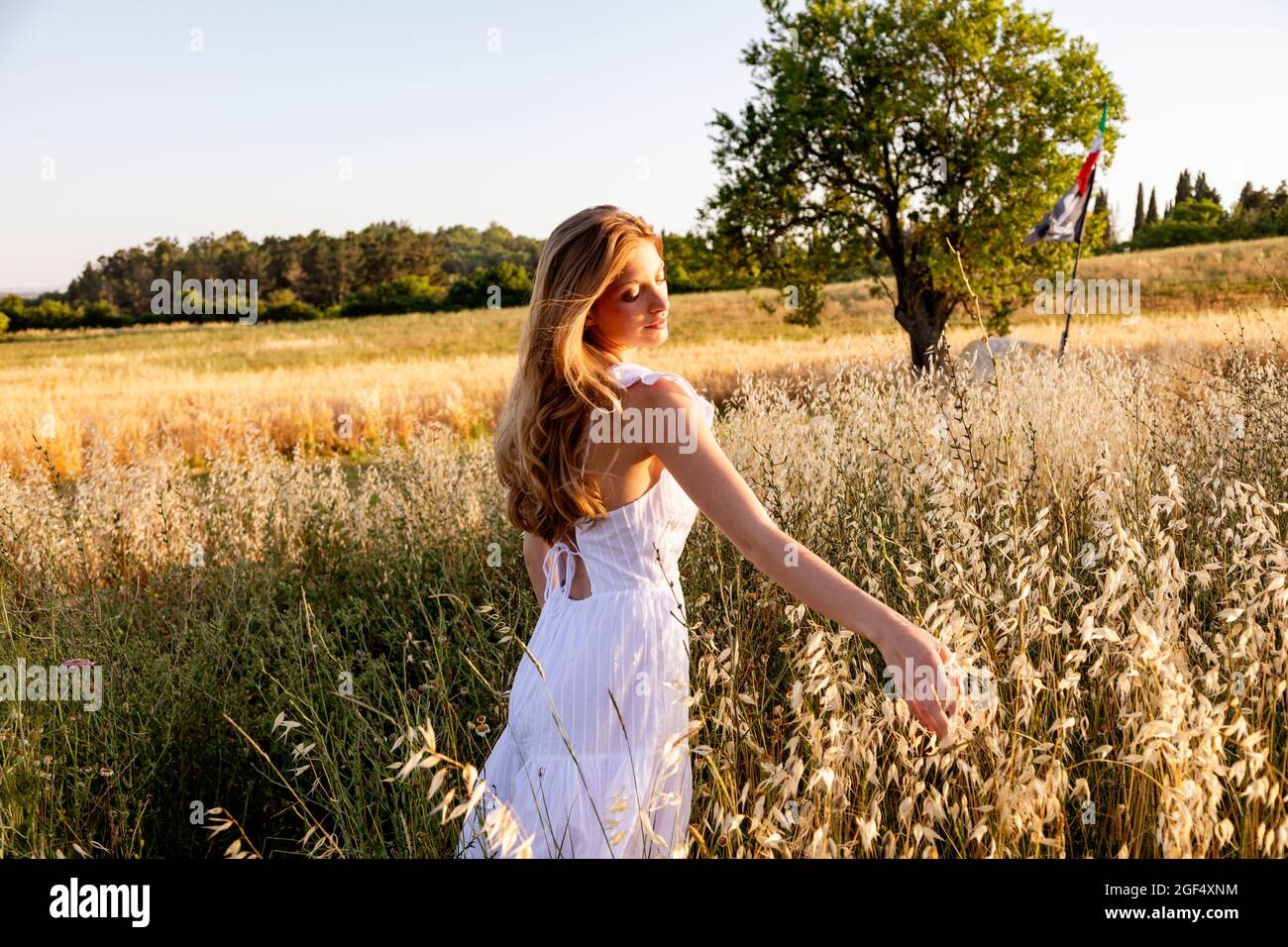 Bella donna in abito bianco che tocca le piante sul campo Foto Stock