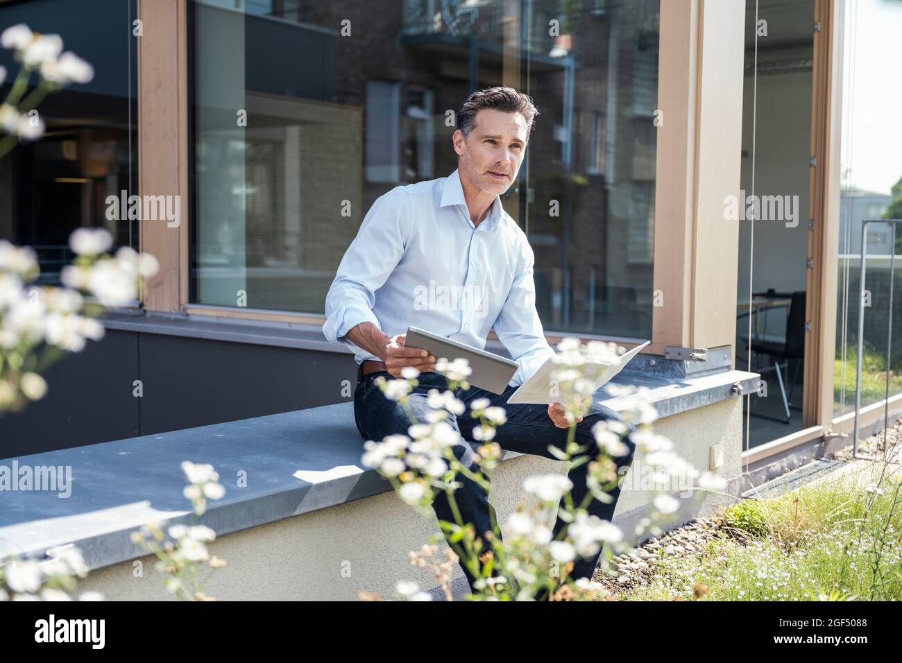 Uomo d'affari con tablet e documenti digitali che guardano lontano Foto Stock