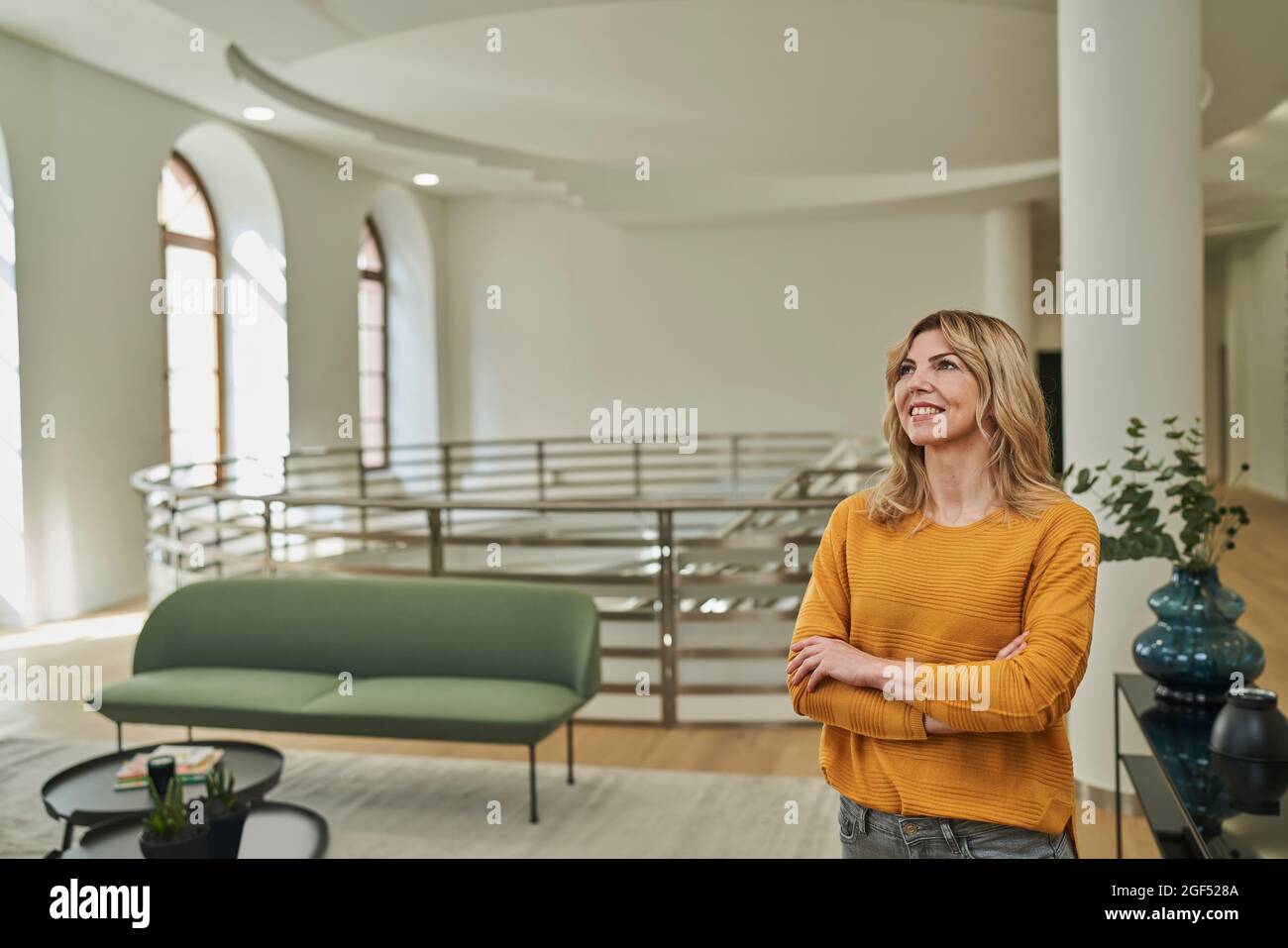 Una giornata di donne d'affari sogna mentre si alza con le braccia incrociate nella lobby dell'ufficio Foto Stock