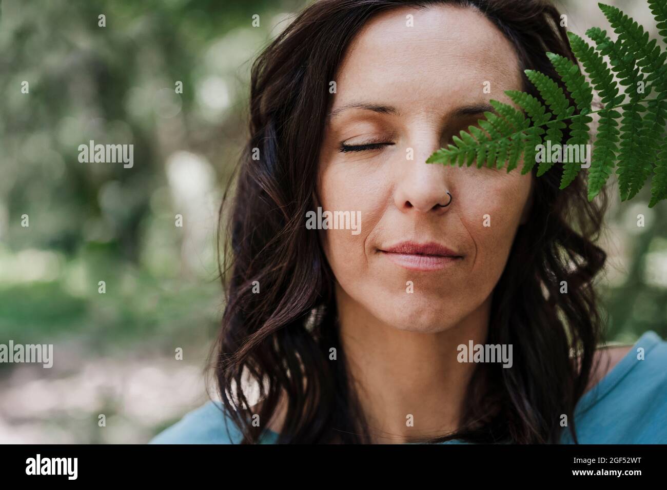 Donna con occhi chiusi tenendo foglia di felce in foresta Foto Stock