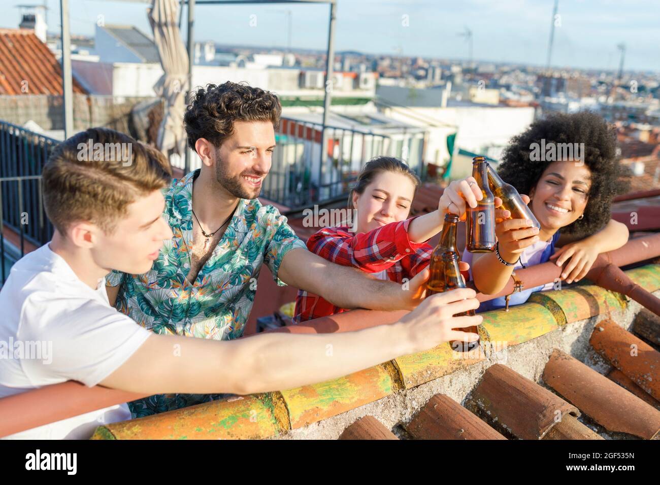 Giovani amici multietnici che tostano bottiglie di birra sul tetto durante il fine settimana Foto Stock