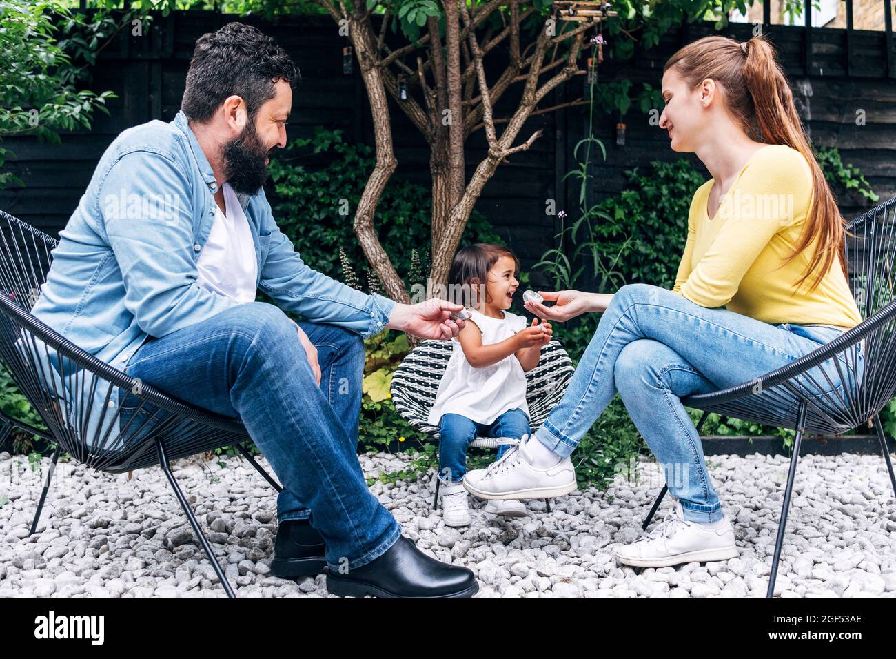 Sorridendo i genitori che tengono i ciottoli mentre si siedono dalla figlia al cortile posteriore Foto Stock