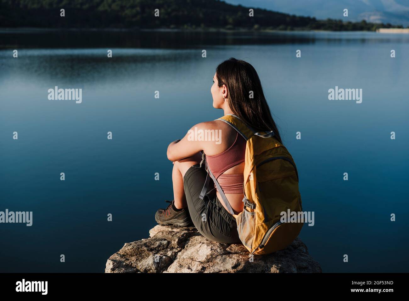 Giovane zaino femminile con zaino seduto su roccia vicino al lago Foto Stock