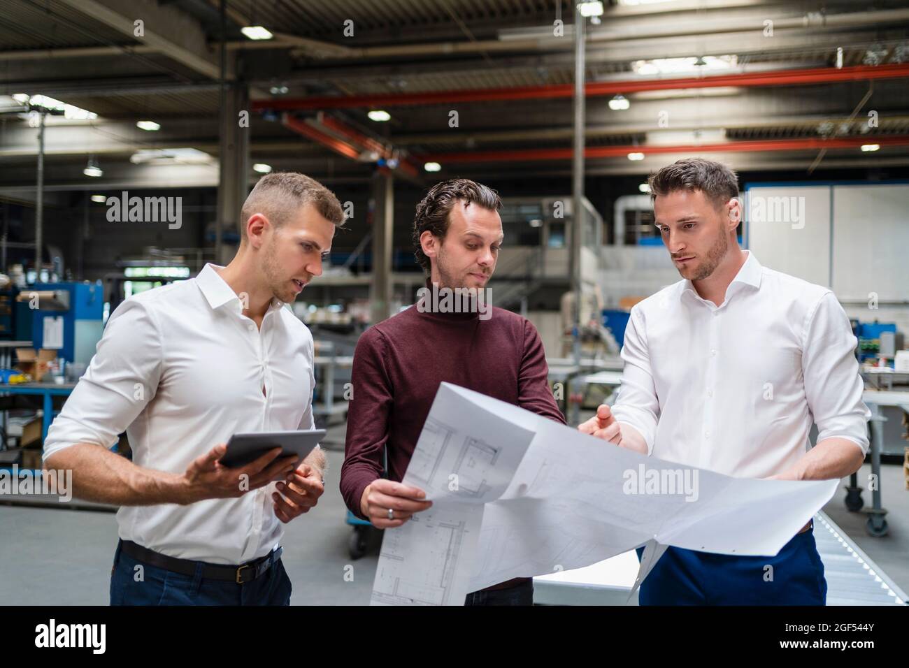 Professionisti di sesso maschile che discutono oltre Blueprint in fabbrica Foto Stock