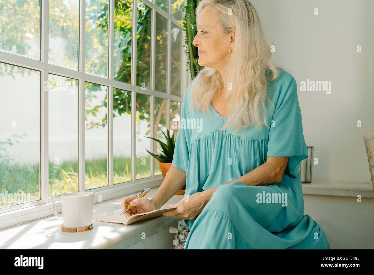 Donna che guarda attraverso la finestra mentre è seduto a casa Foto Stock