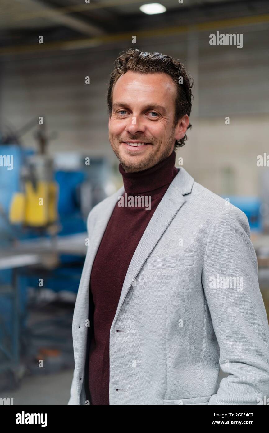 Uomo d'affari sorridente che indossa un blazer grigio all'industria Foto Stock