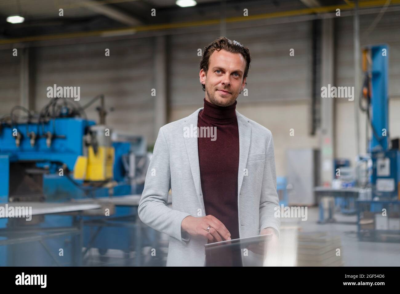 Uomo d'affari in blazer grigio in piedi con tablet digitale in fabbrica Foto Stock