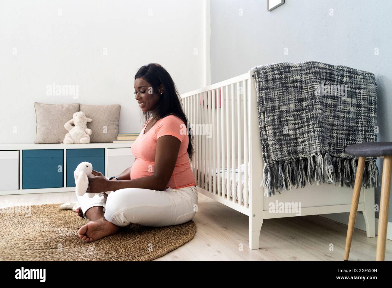 Donna incinta felice guardando animale giocattolo imbottito mentre si siede su tappeto a casa Foto Stock