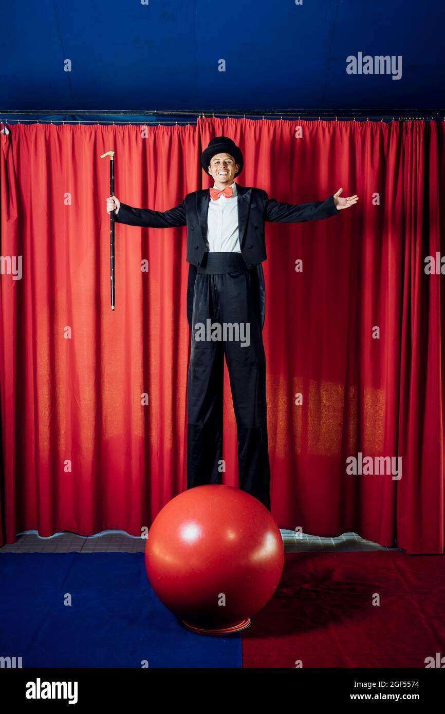 Artista maschile sorridente in piedi con le braccia distese su palafitte al circo Foto Stock