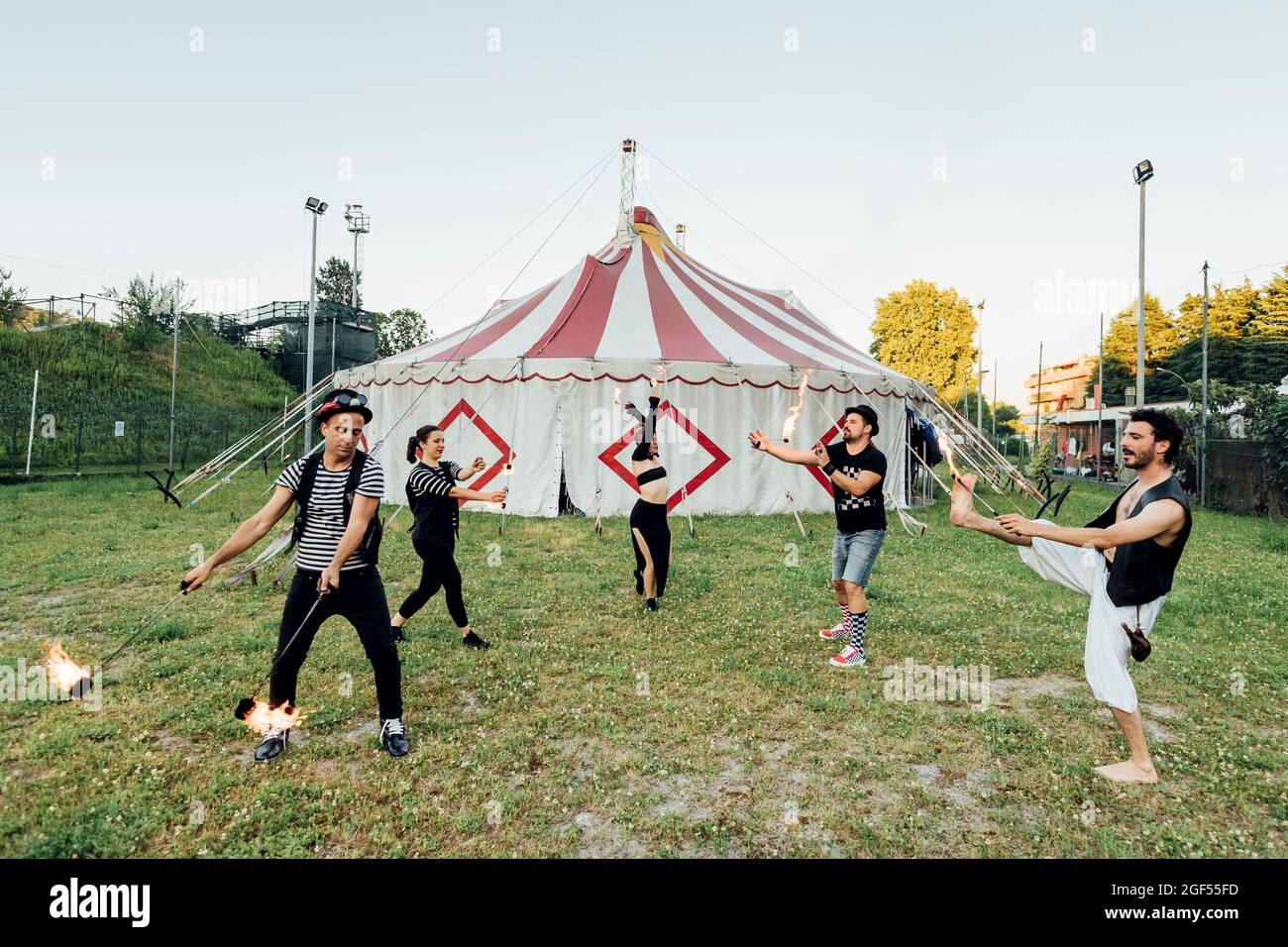 Gli artisti del circo si allenano con attrezzature antincendio mentre si levano in piedi sul prato Foto Stock