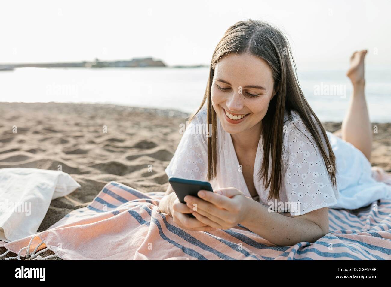 Giovane donna che usa il telefono cellulare mentre si trova su un telo da spiaggia Foto Stock