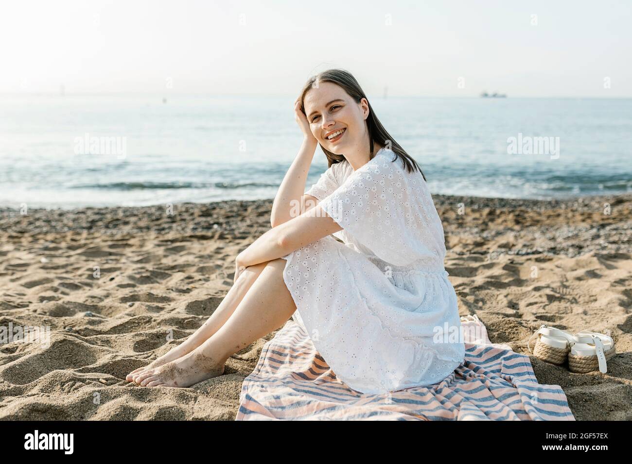 Felice bella donna seduta sul telo da spiaggia Foto Stock