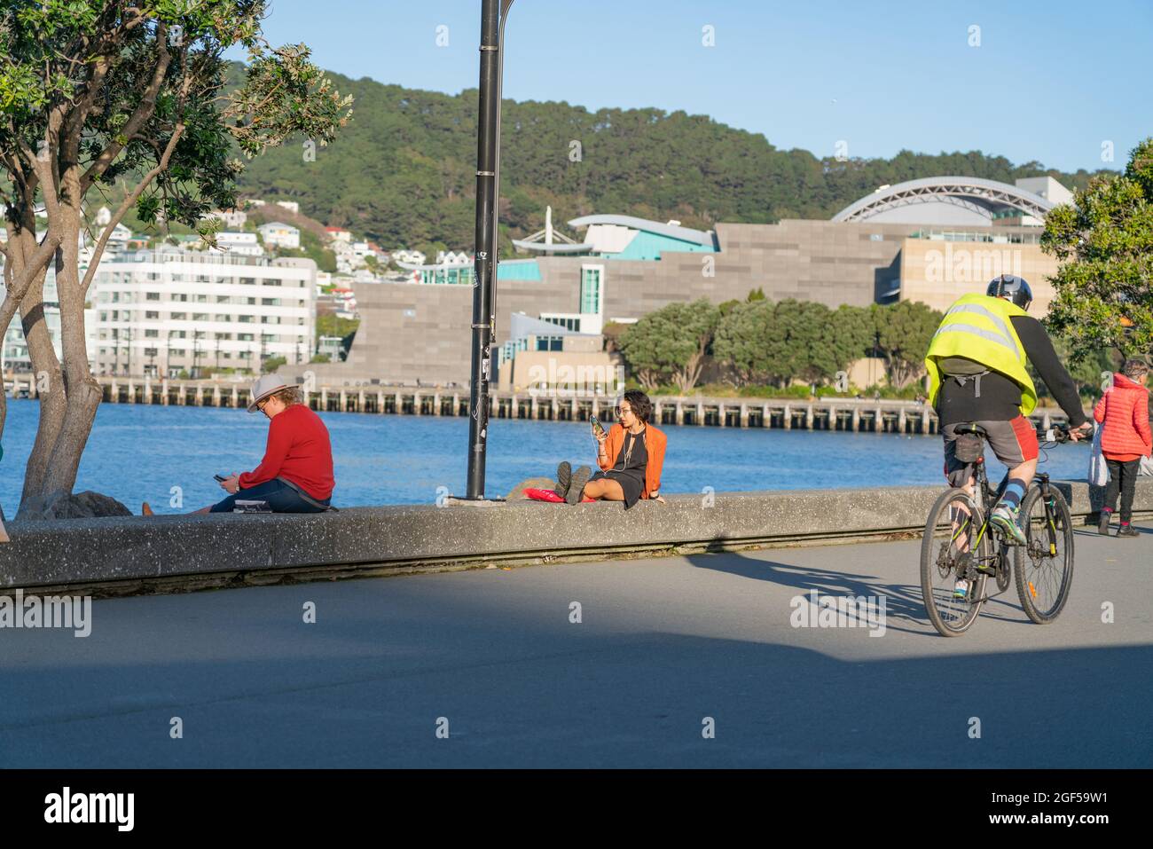 Wellington Nuova Zelanda - Luglio 30 2021; persone che usano dispositivi seduti sul bordo rilassarsi e in bicicletta lungo la Great Harbour Way anche una parte di te Arar Foto Stock