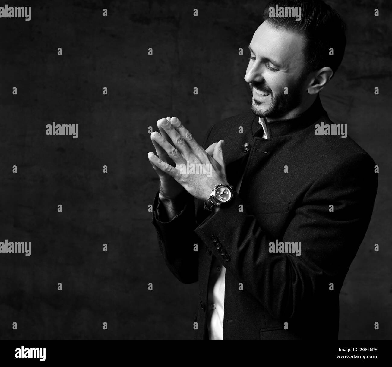 Bianco e nero. L'uomo sorridente non rasato in giacca con colletto di mandarino si alza lateralmente guardando le mani unite Foto Stock