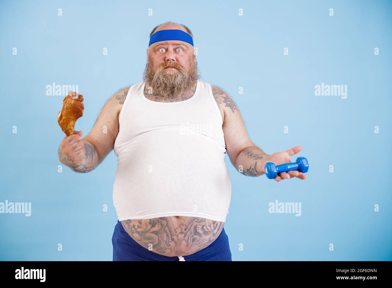 L'uomo confuso con sovrappeso sceglie tra coscia di pollo e manubra su sfondo blu chiaro Foto Stock