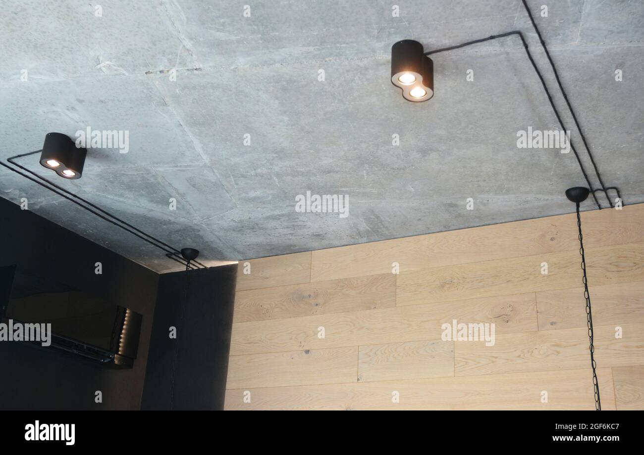 Installazione di moderne ed eleganti luci a binario nere opache, piccole lampade LED a sospensione con cavi neri su un soffitto grigio. Foto Stock