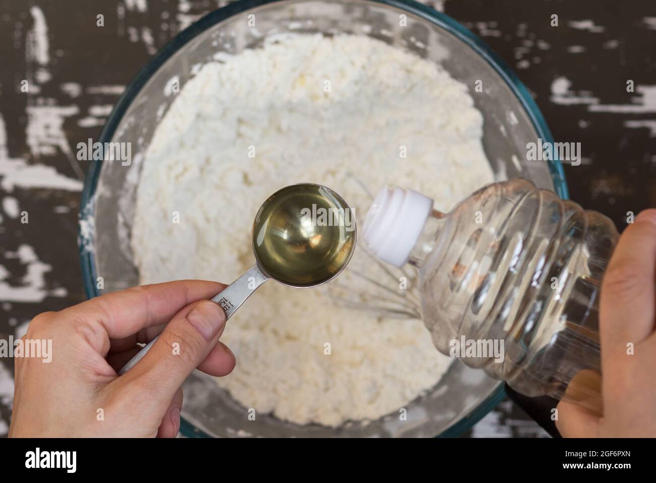 Tavola cucchiaio con olio in mano donna prima di mettere in farina sullo sfondo marrone Foto Stock